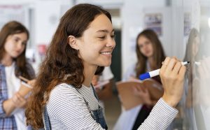 Photo of three High school students, with one drawing on whiteboard