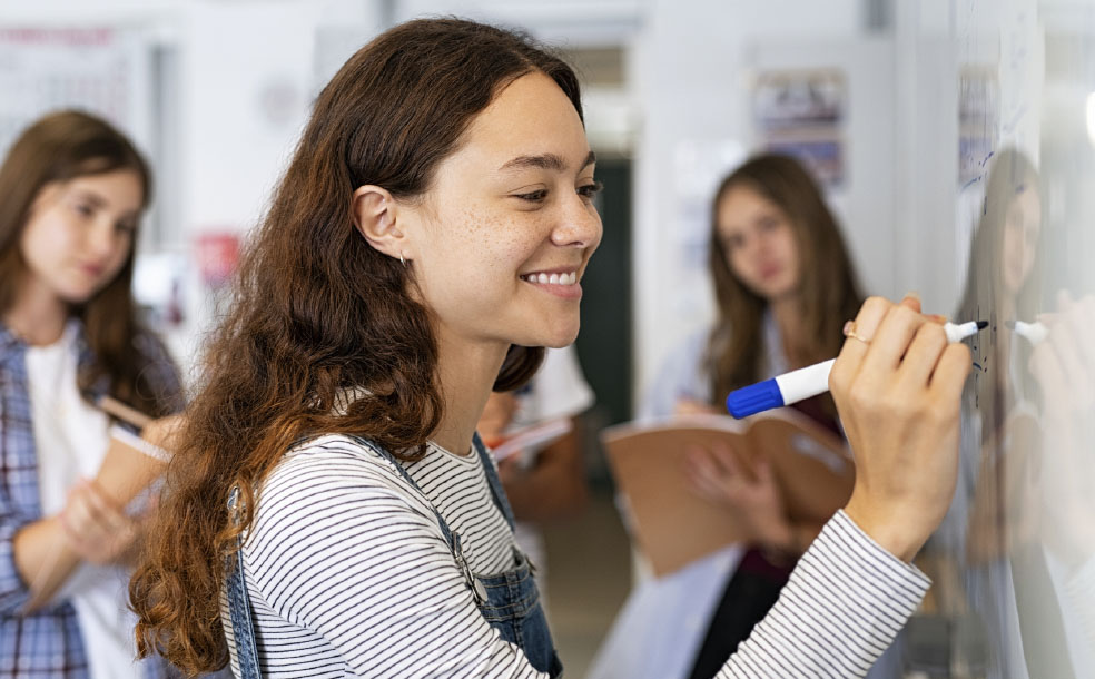 Photo of three High school students, with one drawing on whiteboard